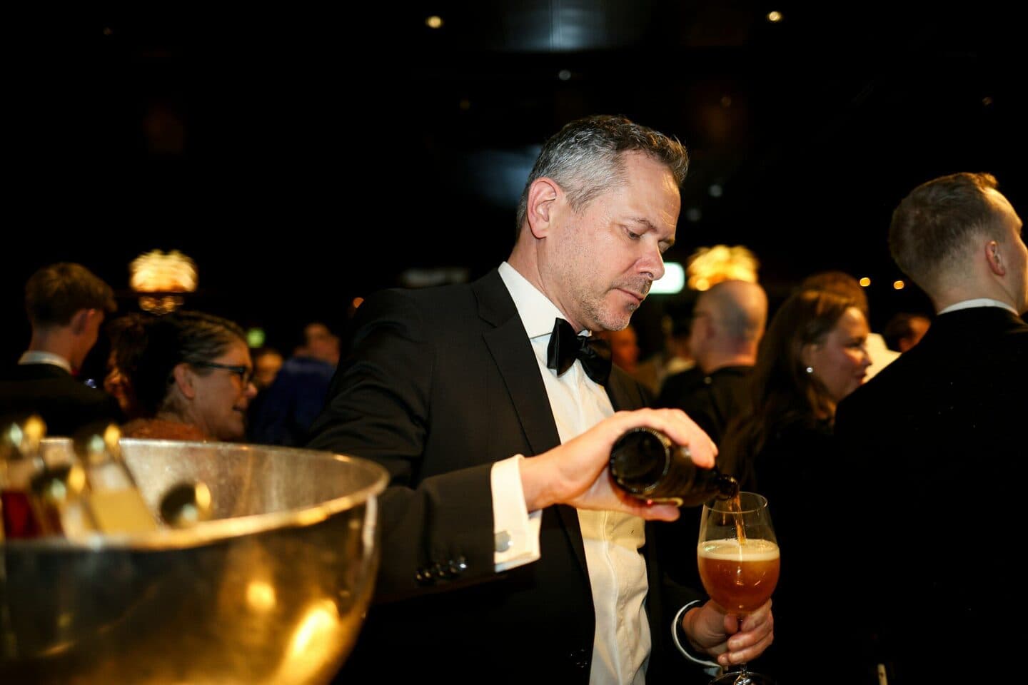 Mann im Smoking schenkt bei einer Gala ein Bier ein